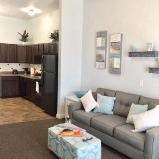 A cozy and modern open-concept living area with a gray sofa and a kitchenette in the background.