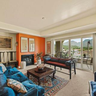 A cozy living room with an orange accent wall, stylish furniture, and large windows offering a mountain view.