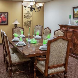 A neatly arranged dining room with a wooden table and upholstered chairs, set with decorative green glasses.