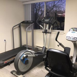 A small indoor gym with a treadmill, exercise bike, and elliptical machine.