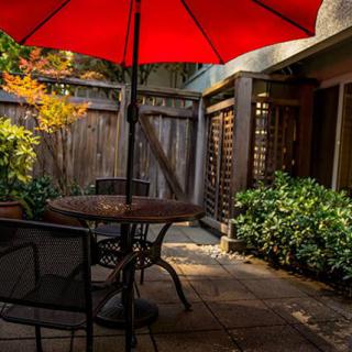 A cozy patio with a red umbrella, surrounded by lush greenery.