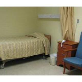 A simple room with a single bed, a blue chair, and a wooden nightstand.