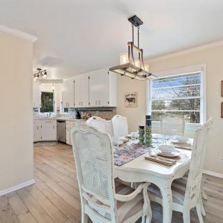 A bright and modern dining area with a view into a stylish kitchen, featuring white furniture and elegant lighting.