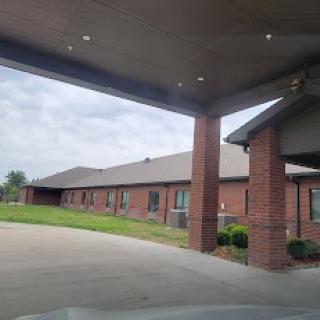 A view of a brick residential building with a covered entrance, set against a cloudy sky.