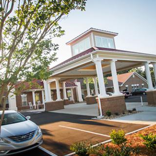 A modern building with a welcoming entrance, surrounded by greenery and vehicles.