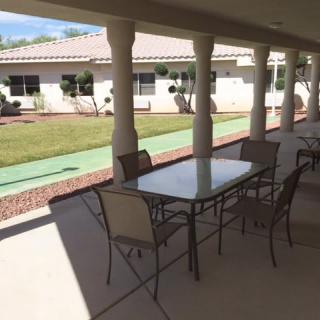 A covered outdoor patio area with a table and chairs, overlooking a garden.