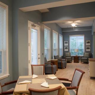 A modern dining area with tables and chairs, lit by natural light through large windows.
