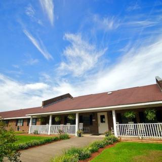 A charming house with a spacious porch and a beautiful garden under a clear blue sky.