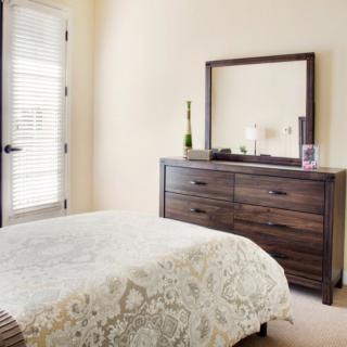 A neatly arranged bedroom featuring a bed and a dresser with a mirror.