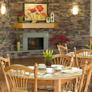 A cozy dining room with a brick fireplace, decorated with wooden furniture and a floral painting.