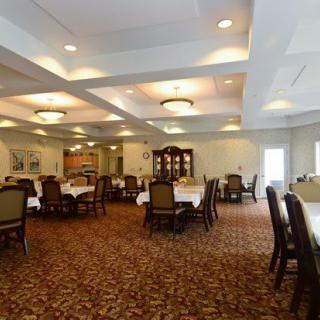 A well-lit dining room with neatly arranged tables and chairs, featuring a patterned carpet and elegant lighting fixtures.
