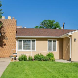 A single-story house with a well-maintained lawn and brick chimney under a clear blue sky.