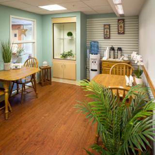 A cozy waiting room with wooden tables and chairs, plants, and a water cooler.