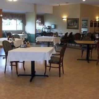 An empty dining area with neatly arranged tables and chairs, each table covered with a white tablecloth.