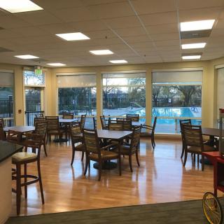 An empty dining area with tables and chairs, featuring large windows and wood flooring.