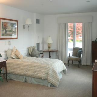 A cozy bedroom featuring a single bed with striped bedding, armchairs, and large windows providing natural light.