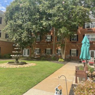 A peaceful garden area with a fountain, surrounded by trees and a multi-story building.