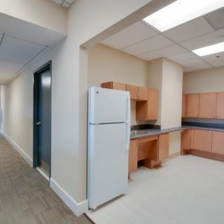 A compact office kitchen area with a refrigerator and wooden cabinets.