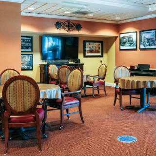 A cozy dining area with round tables and elegant chairs set on a carpeted floor, decorated with wall art.