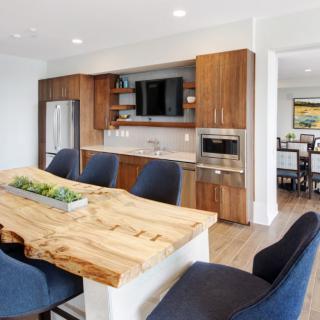 A modern kitchen and dining area with a wooden table, dark chairs, and stainless steel appliances.