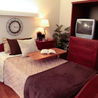 A cozy bedroom featuring a neatly arranged layout with a television, decorative pillows, and warm lighting.