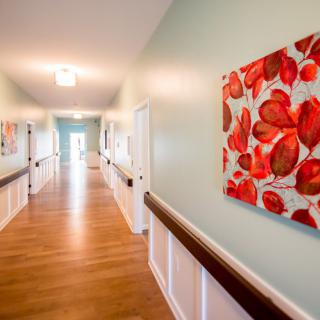 A brightly lit hallway with decorative paintings and a wooden floor.