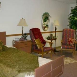 A cozy bedroom with a bed, chairs, lamps, and decorative plants.