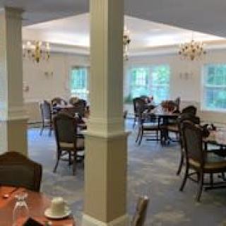 A spacious dining room with multiple tables and chairs, featuring chandeliers and large windows.