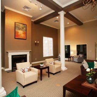 A spacious living room with a fireplace, armchairs, and a coffee table, featuring high ceilings and decorative pillars.