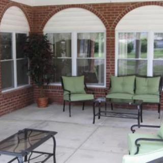 Outdoor patio area with green cushioned seating and a potted plant against a brick wall.