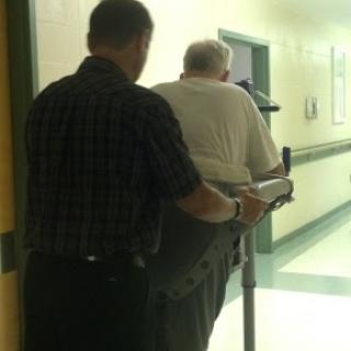 A caregiver assisting an elderly person with a walking aid in a healthcare facility.