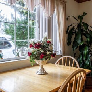 A cozy dining area with a wooden table, adorned with a floral centerpiece, and bathed in natural light from the large window.