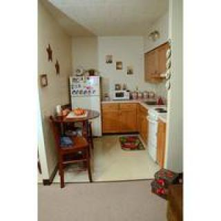 A cozy, compact kitchen area in an apartment with a small dining table, refrigerator, microwave, and wooden cabinets.