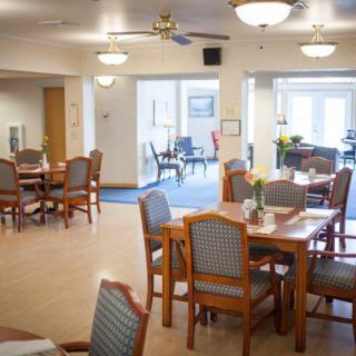 A bright and spacious dining area with several tables and chairs arranged neatly, featuring ceiling fans and soft lighting.