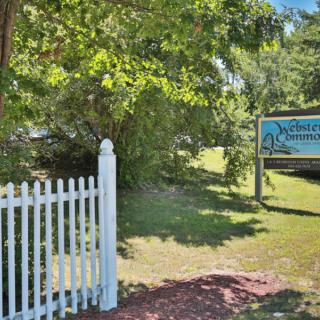 A wooden sign along a white picket fence in a lush, green garden setting.