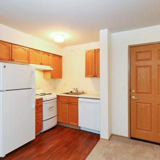 A compact apartment kitchen with wooden cabinets and white appliances.