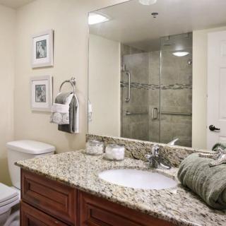 A well-organized bathroom featuring a granite countertop, a large mirror, and a glass-enclosed shower.