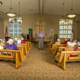 A pastor addressing the congregation inside a church with stained glass windows.