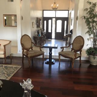 A cozy living room with elegant chairs and a small table, featuring hardwood floors and a chandelier near the entrance.