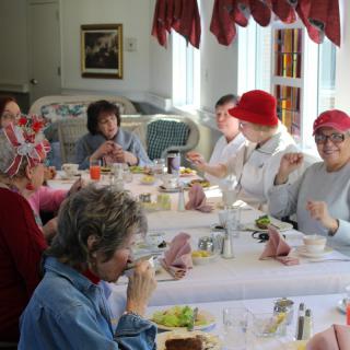 A group of people enjoying a meal together indoors, many wearing decorative hats.