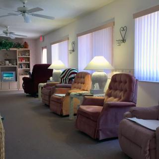 A cozy living room with a row of armchairs, side tables with lamps, and sunlight filtering through vertical blinds.