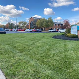 A well-maintained grassy area in front of a building with a clear blue sky and clouds.