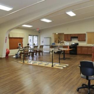 A spacious rehabilitation room equipped with physical therapy equipment and a kitchen area.