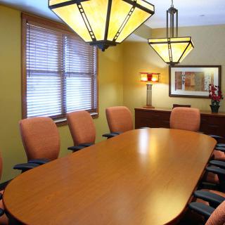 A modern conference room with a long wooden table, surrounded by several orange chairs and illuminated by stylish overhead lights.