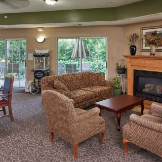 A cozy living room with upholstered furniture, a fireplace, and large windows overlooking greenery.