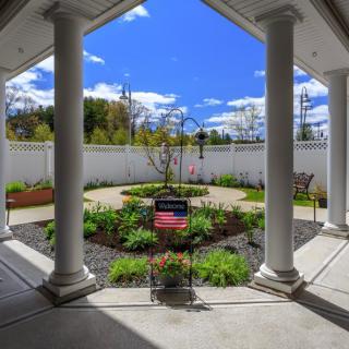 A beautifully landscaped garden viewed from a covered patio with large columns and a bright blue sky overhead.