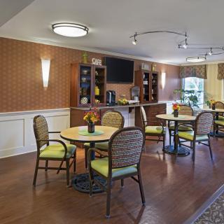 A cozy dining area with neatly arranged tables and chairs, featuring warm lighting and elegant wall decor.