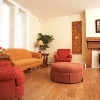 A cozy living room with a warm color palette featuring a sofa, armchair, and ottoman on hardwood flooring.