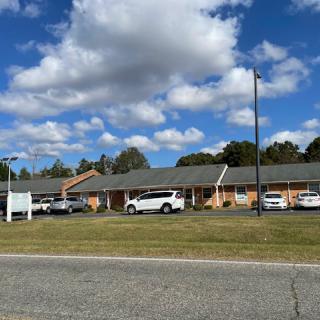 A row of buildings with a parking lot and several parked cars under a partly cloudy sky.