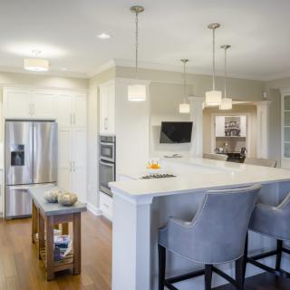 A modern kitchen with a sleek island counter, stainless steel appliances, pendant lighting, and comfortable bar stools.